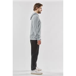 A side view of a man wearing a grey pullover hoody with a hood, paired with black pants and white shoes.