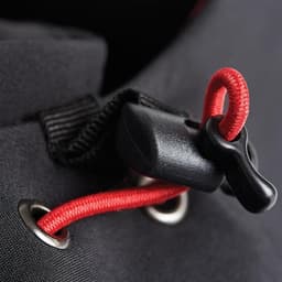 A close-up of a black softshell jacket featuring a red drawcord and toggle. The fabric has metallic eyelets.