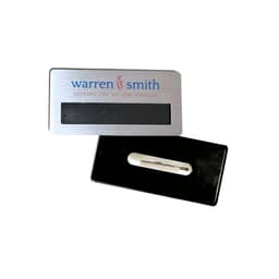 A silver DIY staff badge with a magnet on the back and a black surface for inserting details. It has a logo.