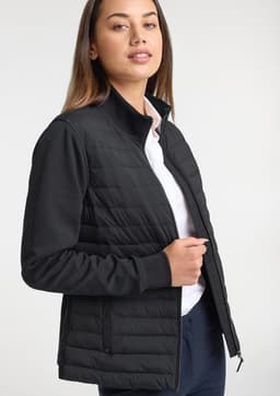 A women's tailor jacket in black, featuring a quilted design and a zip closure. A model is wearing it with a white shirt.