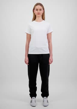 A woman in a white t-shirt and black track pants stands against a plain background. The pants have a branding logo.