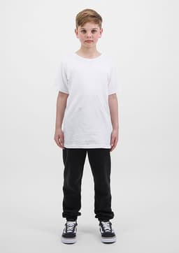 A child stands wearing a plain white t-shirt and black track pants, complemented by black and white sneakers.