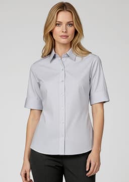 A woman models a short-sleeve button-up shirt in light blue, featuring a collar and a subtle striped pattern.