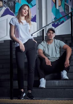 A woman in a white T-shirt and a man in a grey T-shirt sit on black stairs, both wearing casual athletic attire.