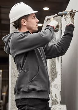A grey unisex zip front multi-pocket hoodie worn by a worker using a tool, with a safety helmet and gloves.