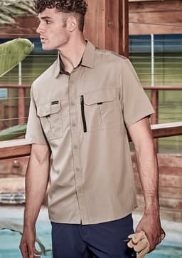 A tan short sleeve button-up shirt with two front pockets and a zip pocket, worn by a male model.