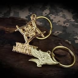 A gold-coloured die struck 2D key chain featuring intricate designs and a key ring. It includes a logo.