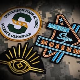 Four embroidered patches on a camouflaged background, featuring various designs and colours, including blue, yellow, and white.