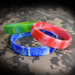 Three silicone wristbands in blue, red, and green swirl patterns, featuring embossed text and a logo.