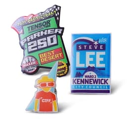 A collection of three brightly coloured lapel pins featuring various designs and logos, including a racing theme and a city council vote.