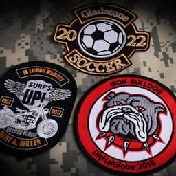 Three embroidered patches displayed on a camouflaged background, featuring various designs and colours, including a soccer patch.