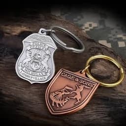 Two die struck 2D key chains in silver and bronze, featuring intricate designs and circular key rings.
