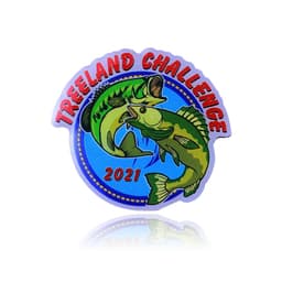 A circular lapel pin featuring two fish on a blue background with "Treeland Challenge 2021" written in bold red letters.