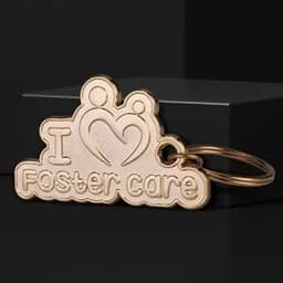 A gold die struck 2D key chain featuring the phrase "I ♥ Foster care" and a logo.