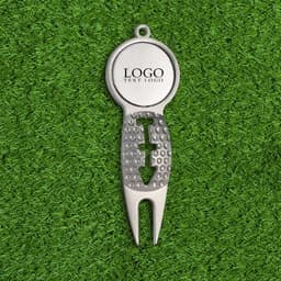 A silver golf divot tool featuring a circular top and a textured grip, set against a green grass background.