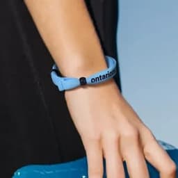 An adjustable double-layer friendship bracelet in light blue, featuring a black logo, worn on a wrist.