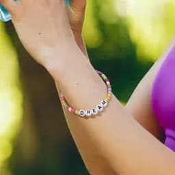 A colourful elastic bracelet featuring letter beads spelling "DREAM" and various pastel hues.