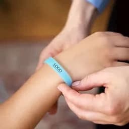 A blue glow in the dark silicone bracelet being placed on a wrist, with a hand assisting.