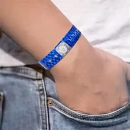 A blue disposable laser holographic identification bracelet is worn on a wrist, featuring a circular attachment.