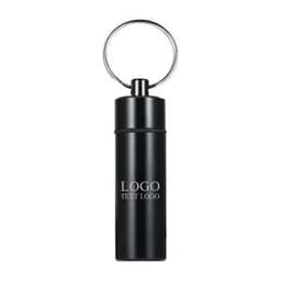 A black waterproof pill box keychain with a silver keyring and a logo on the surface.