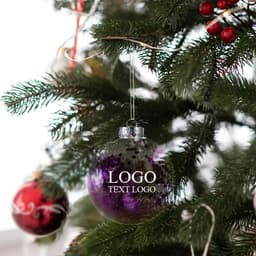 A purple and silver shatter-resistant ornament hanging on a Christmas tree amidst green branches and red decorations.