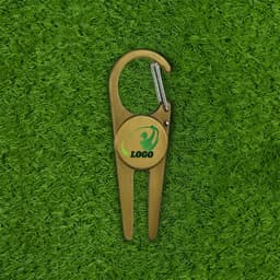 A gold golf divot tool with a clip hook, featuring a circular area for a logo, placed on green grass.