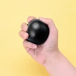 A black jewel-shaped stress ball is being squeezed in a hand against a yellow background.