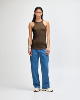 A woman wearing an olive green racerneck tank top and loose blue cargo jeans, standing with a relaxed pose.
