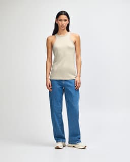 A light beige women's racerneck tank top, paired with loose-fitting denim jeans and white sneakers, featuring a logo.