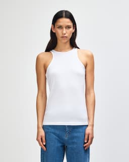 A white women's racerneck tank top with a fitted design, displayed on a model. It features a branding logo.
