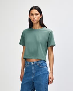 A model wearing a green boxy t-shirt, with short sleeves and loose fit, paired with light denim jeans.