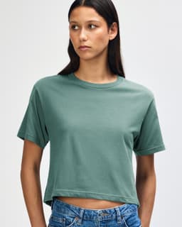 A woman wearing a teal boxy t-shirt, styled with light blue denim shorts. The shirt has a logo.