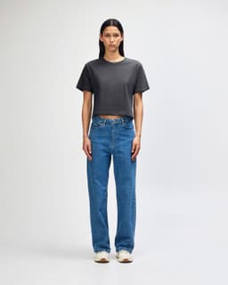 A woman wearing a grey boxy t-shirt and light blue cargo jeans, paired with black and white sneakers.
