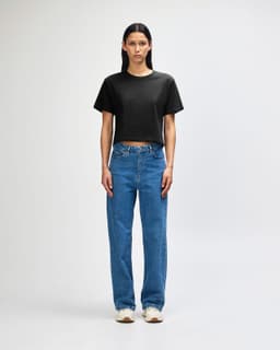 A woman wearing a black boxy T-shirt and wide-leg blue jeans, standing against a white background.