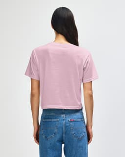 A back view of a pink boxy t-shirt with short sleeves, paired with light blue denim jeans. The shirt features a logo.