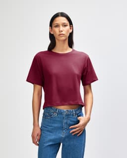 A boxy maroon T-shirt is displayed on a model, paired with light blue jeans. The shirt has a logo.