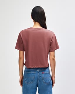 A woman with curly hair wearing a dusty rose boxy t-shirt, viewed from the back, with light blue cargo pants.