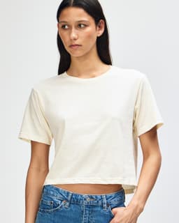 A light cream women's boxy t-shirt displayed on a model, featuring a logo on the garment.