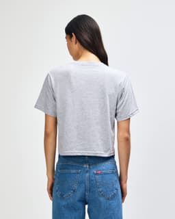 A women’s grey boxy t-shirt with a crew neck, displayed from the back, paired with blue jeans.