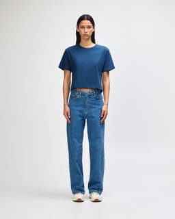 A woman stands wearing a navy blue boxy T-shirt and light blue cargo pants, paired with black and white sneakers.