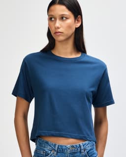 A navy blue boxy t-shirt with short sleeves, displayed on a model with curly hair. The shirt has a logo.