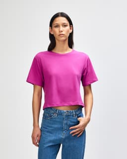 A vibrant fuchsia women's boxy T-shirt with a relaxed fit, paired with light blue jeans. Features a branding logo.