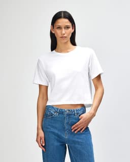 A white boxy T-shirt featuring short sleeves, paired with blue jeans, and has a logo on it.