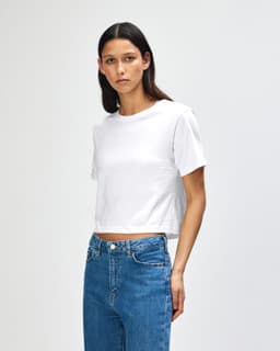 A white women's boxy t-shirt with short sleeves, paired with light blue jeans, featuring a branding logo.