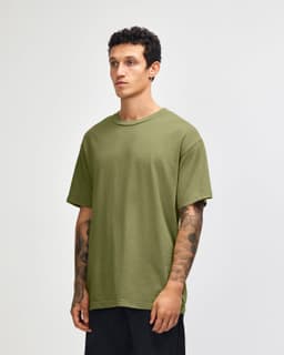 A model wearing an olive green unisex heavyweight cotton T-shirt. The shirt has a relaxed fit and short sleeves.
