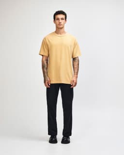 A unisex heavyweight cotton t-shirt in mustard yellow, paired with light blue cargo trousers.