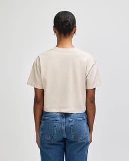 A heavyweight cotton women's crop t-shirt in beige, featuring a boxy fit and branding on the back.
