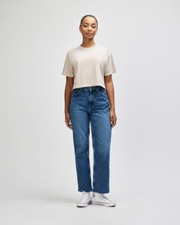 A beige cropped boxy t-shirt paired with blue straight-leg jeans, worn by a model against a plain backdrop.