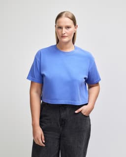 A blue heavyweight cotton women's crop boxy T-shirt worn by a model, featuring a simple design and logo.