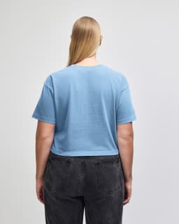 A blue crop boxy t-shirt with a back view, featuring a relaxed fit and short sleeves. There is a logo present.